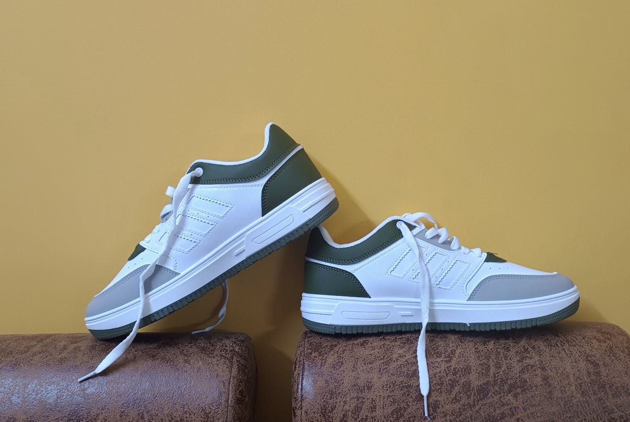about-us White and green casual shoes elegantly displayed against a yellow backdrop, perfect for fashion concepts.