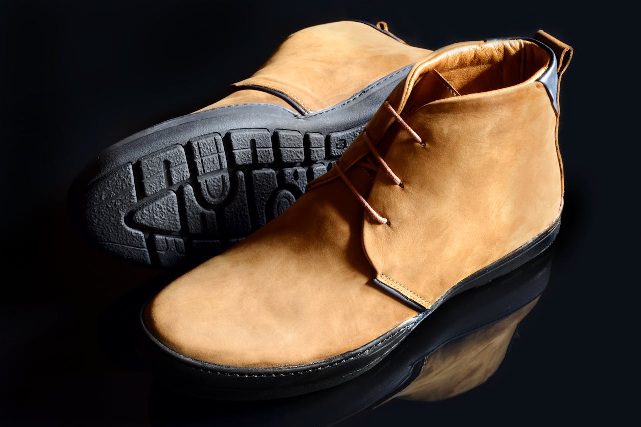 our-story Pair of fashionable leather boots with textured soles on a reflective surface.
