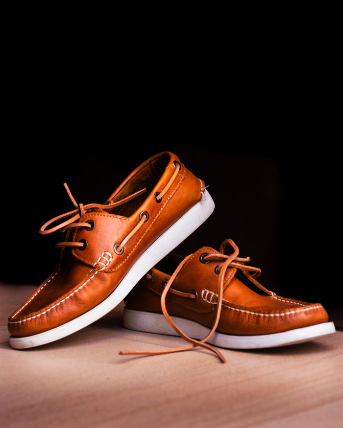 Crafting Captivating Headlines: Your awesome post title goes here Close-up of brown leather boat shoes with white soles on a wooden floor against a black background.